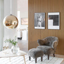 Modernt vardagsrum med ljus askfärgat soffbord, vit mjuk matta, grå fårskinnsfåtölj och fondvägg i ekpanel med två tavlor.